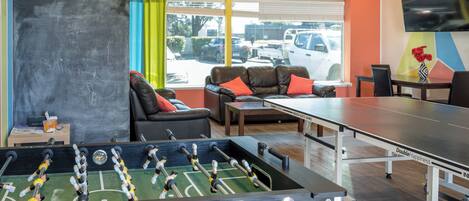 Una habitación con mesa de fútbol, mesa de ping pong, sofá y televisor montado en la pared.
