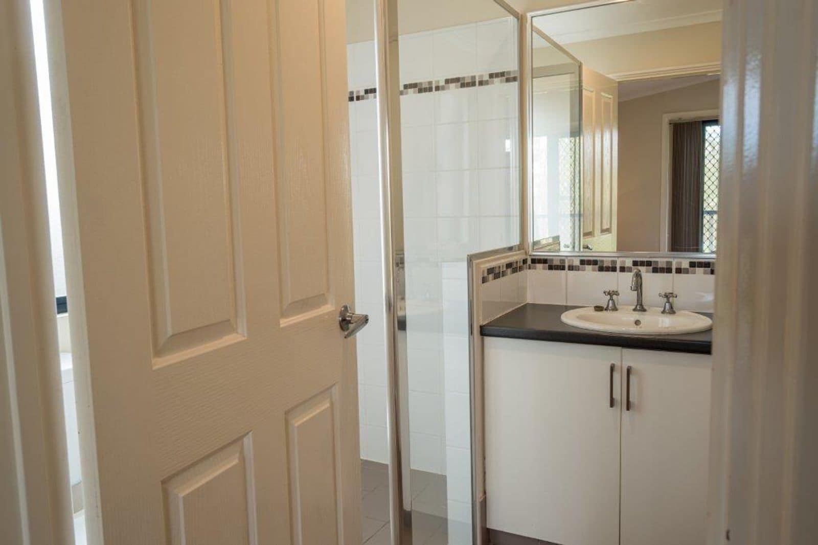 Une salle de bain avec une porte blanche, un lavabo avec un miroir et des murs carrelés.