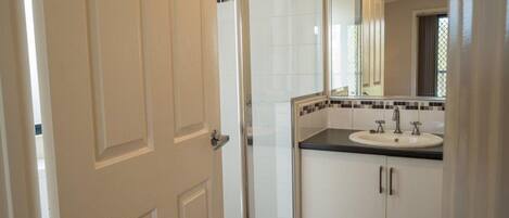 Une salle de bain avec une porte blanche, un lavabo avec un miroir et des murs carrelés.