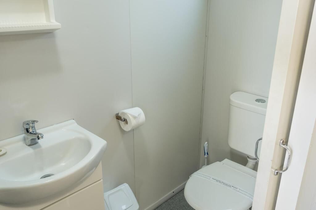 Une petite salle de bain propre, équipée d’un lavabo, de toilettes et d’un porte-rouleau de papier toilette fixé au mur.