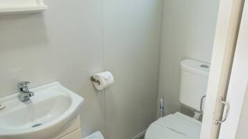 Une petite salle de bain propre, équipée d’un lavabo, de toilettes et d’un porte-rouleau de papier toilette fixé au mur.