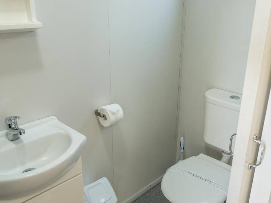 Une petite salle de bain propre, équipée d’un lavabo, de toilettes et d’un porte-rouleau de papier toilette fixé au mur.