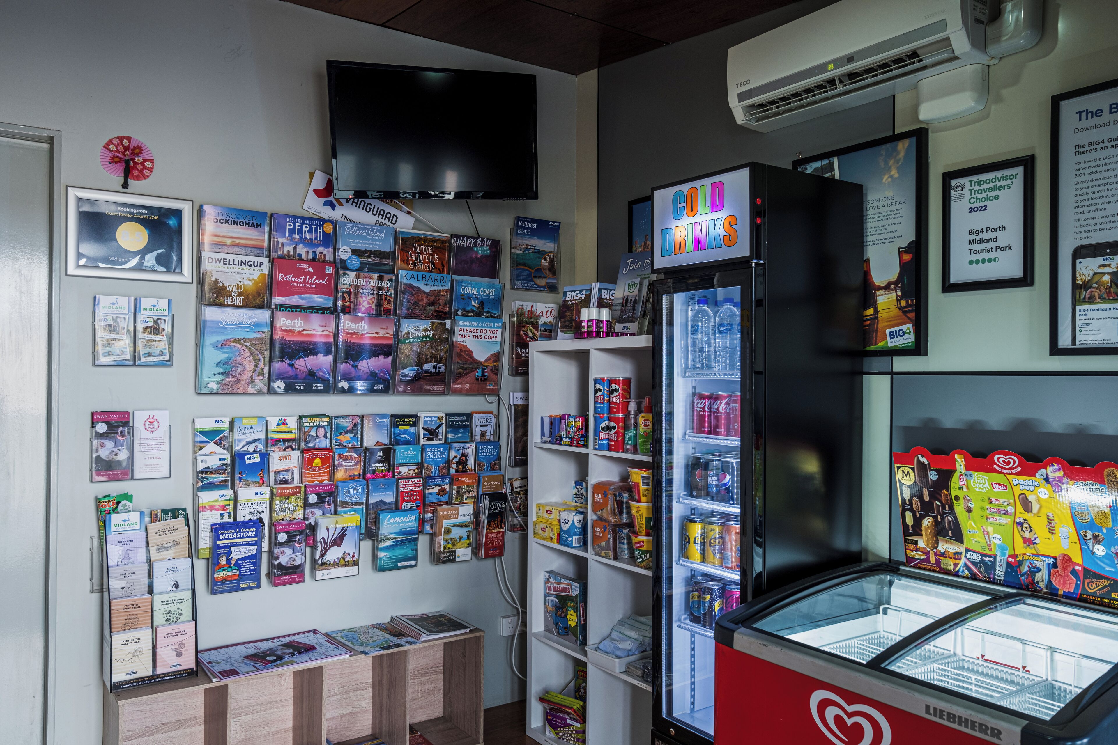 A travel agency with a display of travel brochures, a Liebherr refrigerator, and a mounted television.