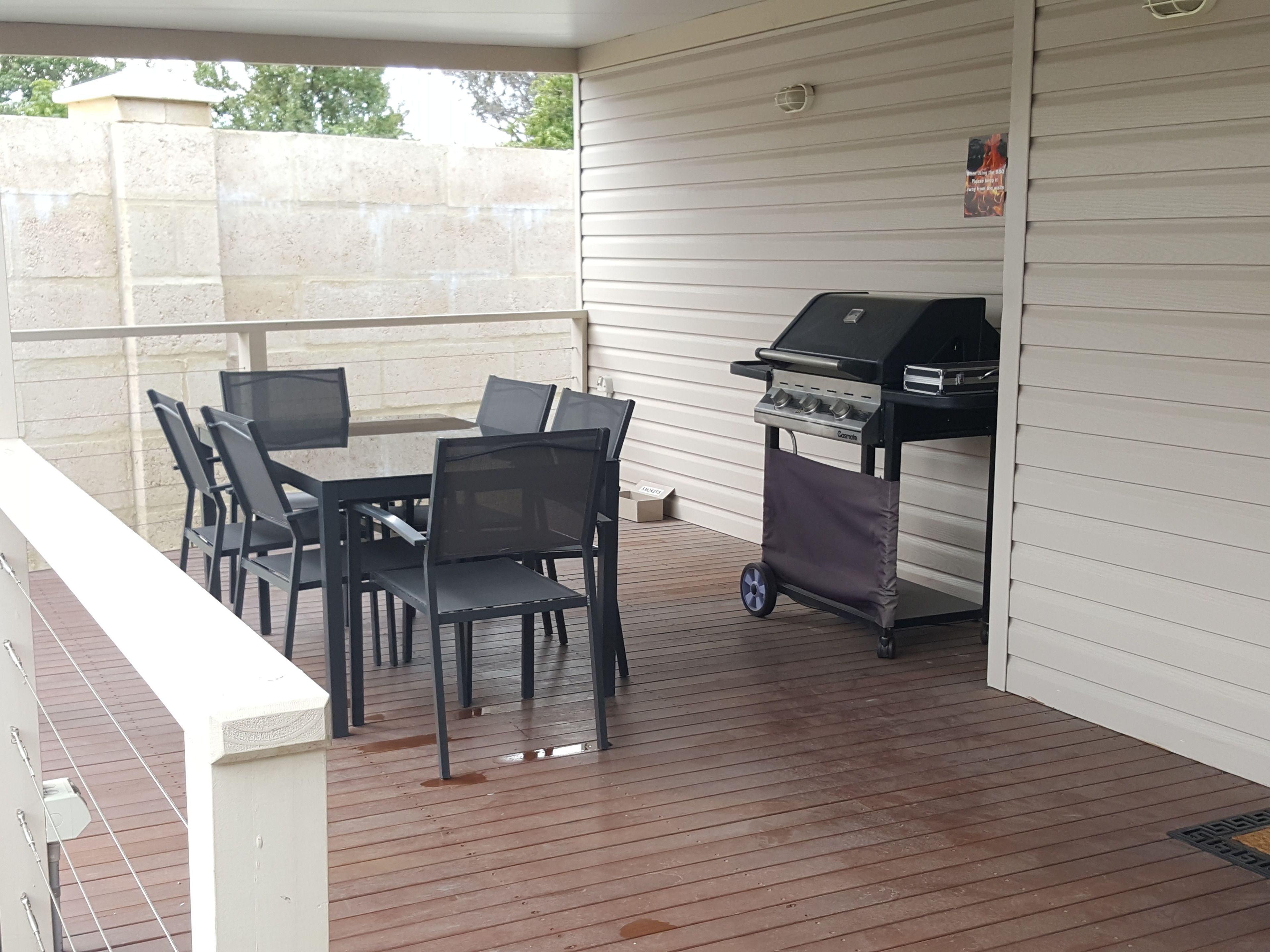 Een terras buiten met een barbecue, een tafel en stoelen.