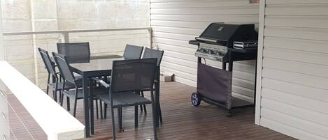 Une terrasse extérieure avec un barbecue, une table et des chaises.
