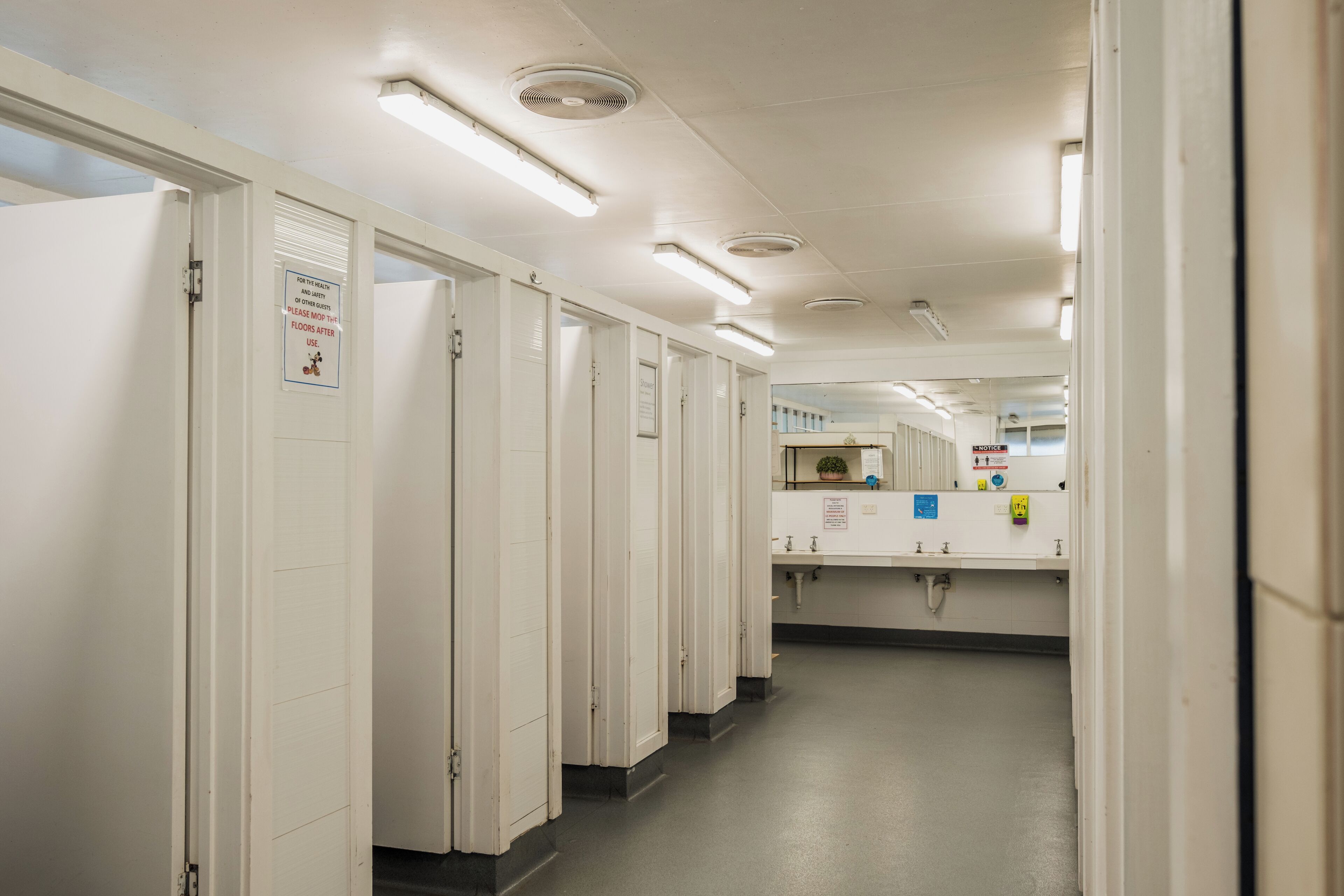 A clean, well-lit hallway with white doors, a sink area, and a sign indicating the use of the floors.