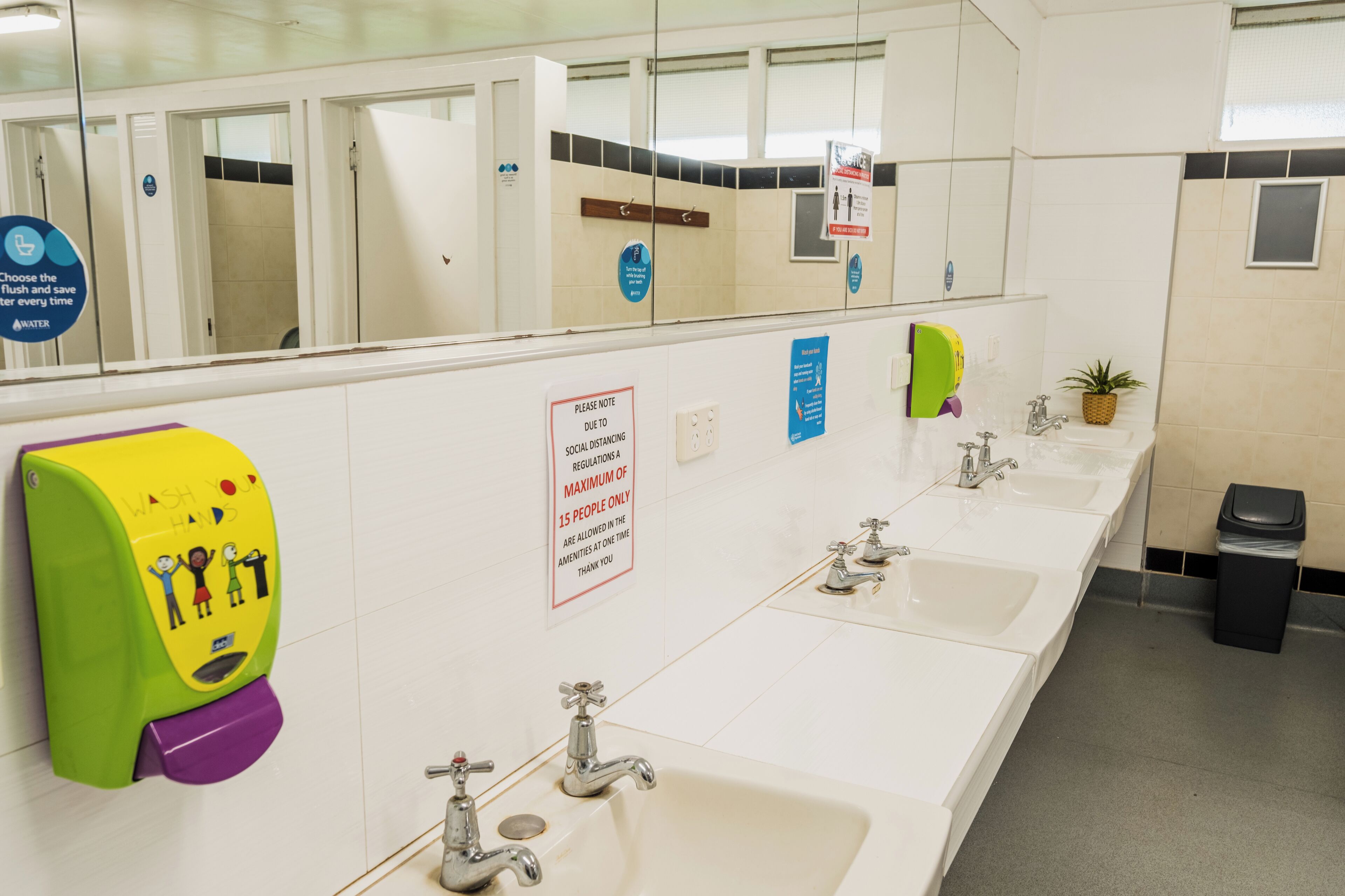 A public restroom with multiple sinks, hand dryers, and a trash bin.