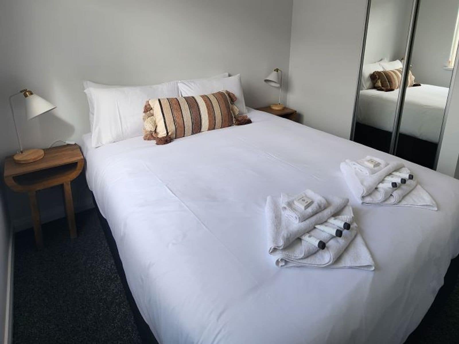 Un lit bien fait, avec des draps blancs, des oreillers à rayures et des serviettes pliées posées sur le lit.