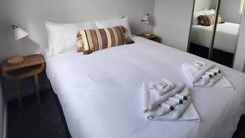 Un lit bien fait, avec des draps blancs, des oreillers à rayures et des serviettes pliées posées sur le lit.