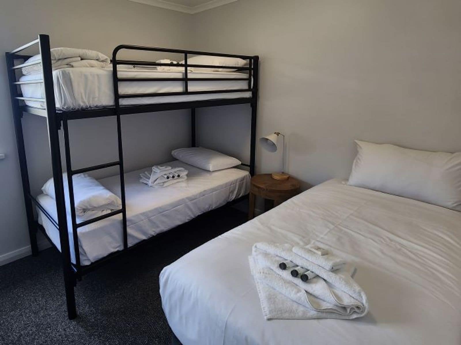 A bunk bed room with a single bed and a nightstand with a lamp.
