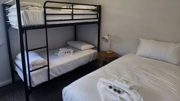 A bunk bed room with a single bed and a nightstand with a lamp.