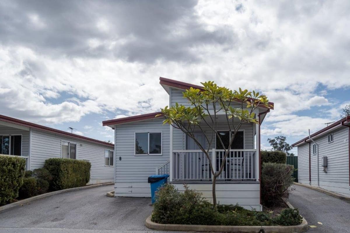 A single-story mobile home with a small porch and a tree in front.