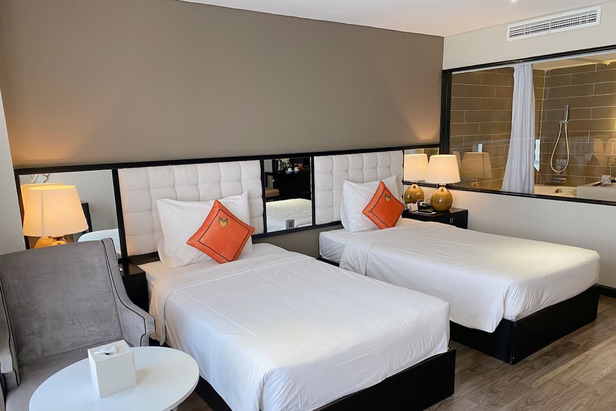 A hotel room with two beds, a small table, a chair, and a mirror.