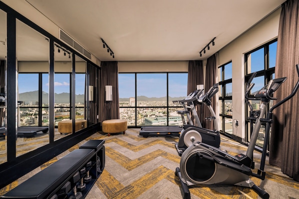 A high-rise hotel gym with treadmills, a bench, and a mirror reflecting the cityscape. - Sanouva Danang Hotel (Da Nang)