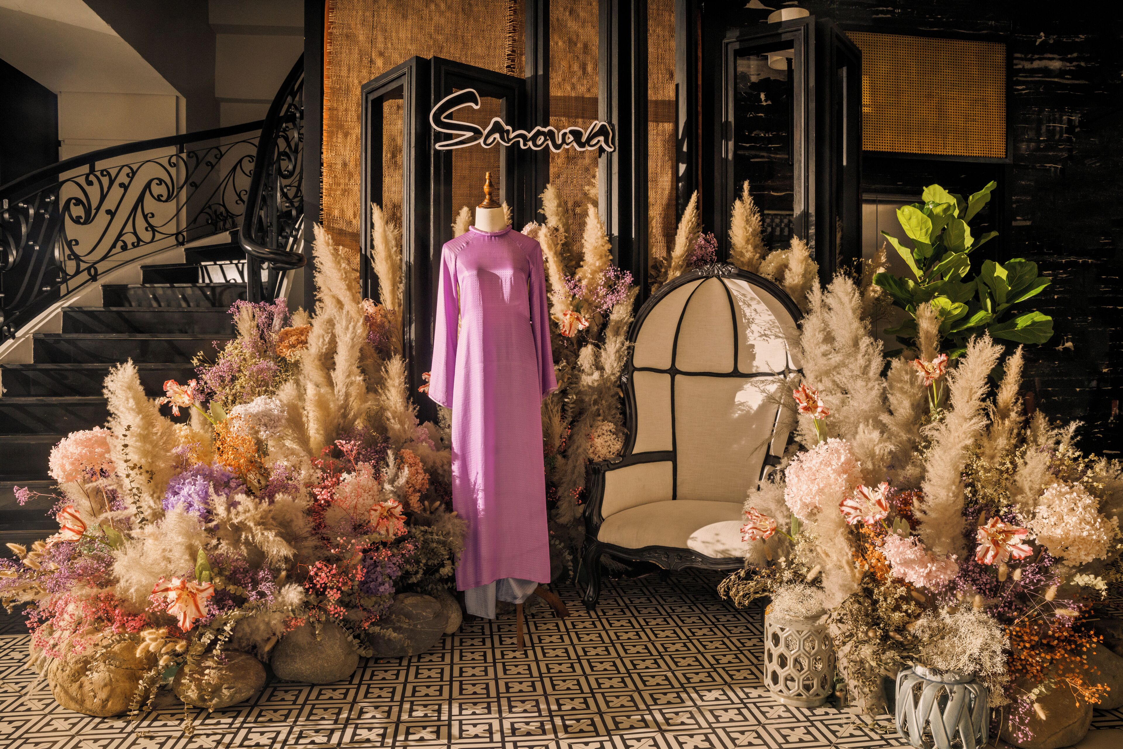 A staircase with a wrought iron railing, a mannequin in a purple dress, and a chair surrounded by decorative plants.