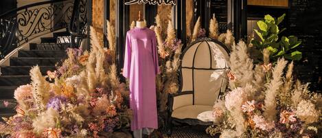 A staircase with a wrought iron railing, a mannequin in a purple dress, and a chair surrounded by decorative plants.
