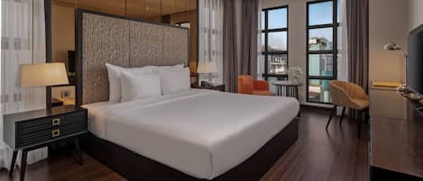 Una habitación de hotel moderna con una cama grande, un escritorio con lámpara, una silla y una televisión.