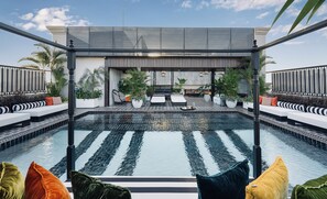 Un área de piscina en la azotea con sillones de descanso y una zona de estar cubierta.