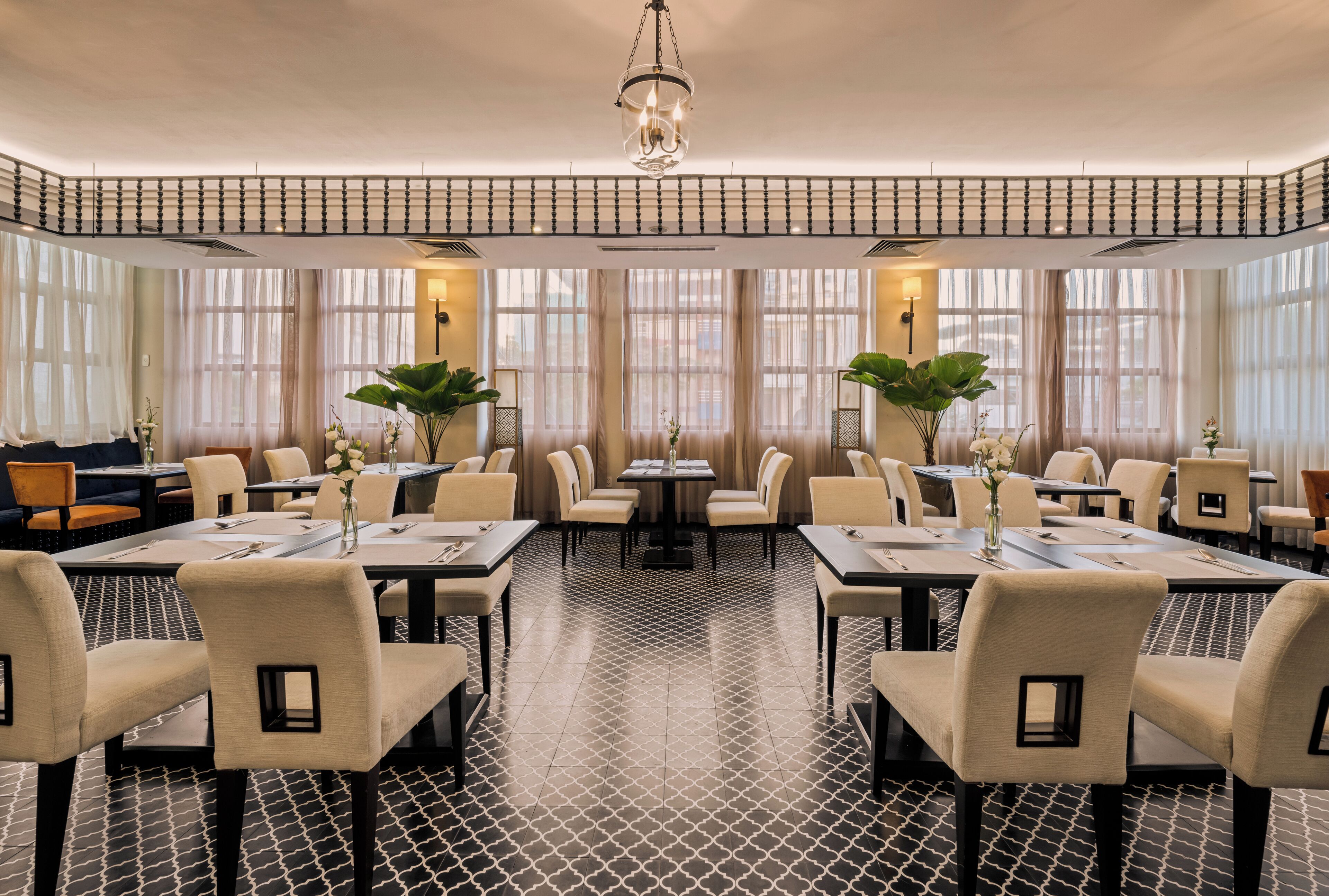 Een restaurant met een geometrisch patoneervloer, ronde tafels met stoelen en grote ramen met transparante gordijnen.