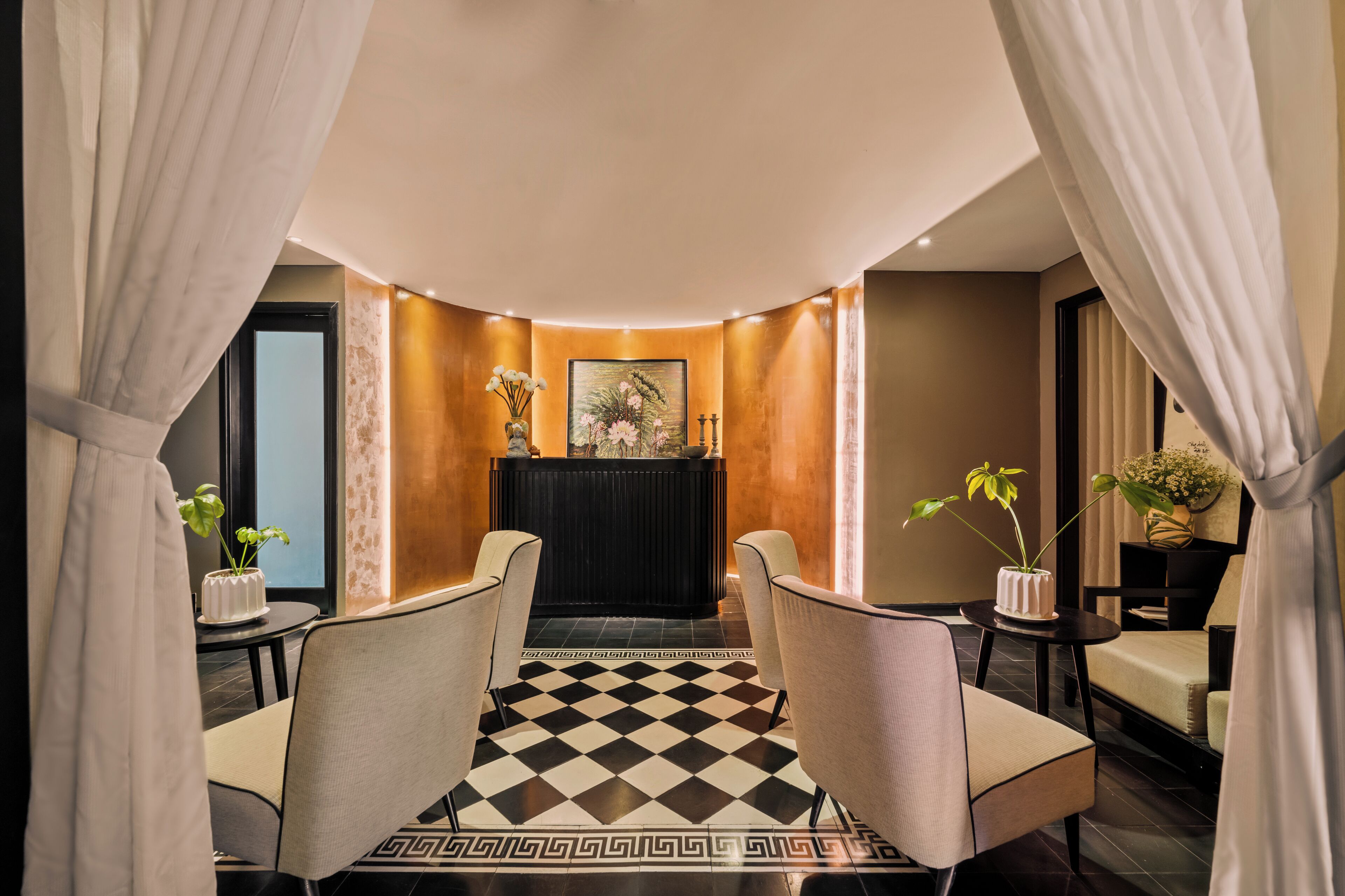 A hotel lobby with a checkered floor, two armchairs, a reception desk, and a vase with flowers.