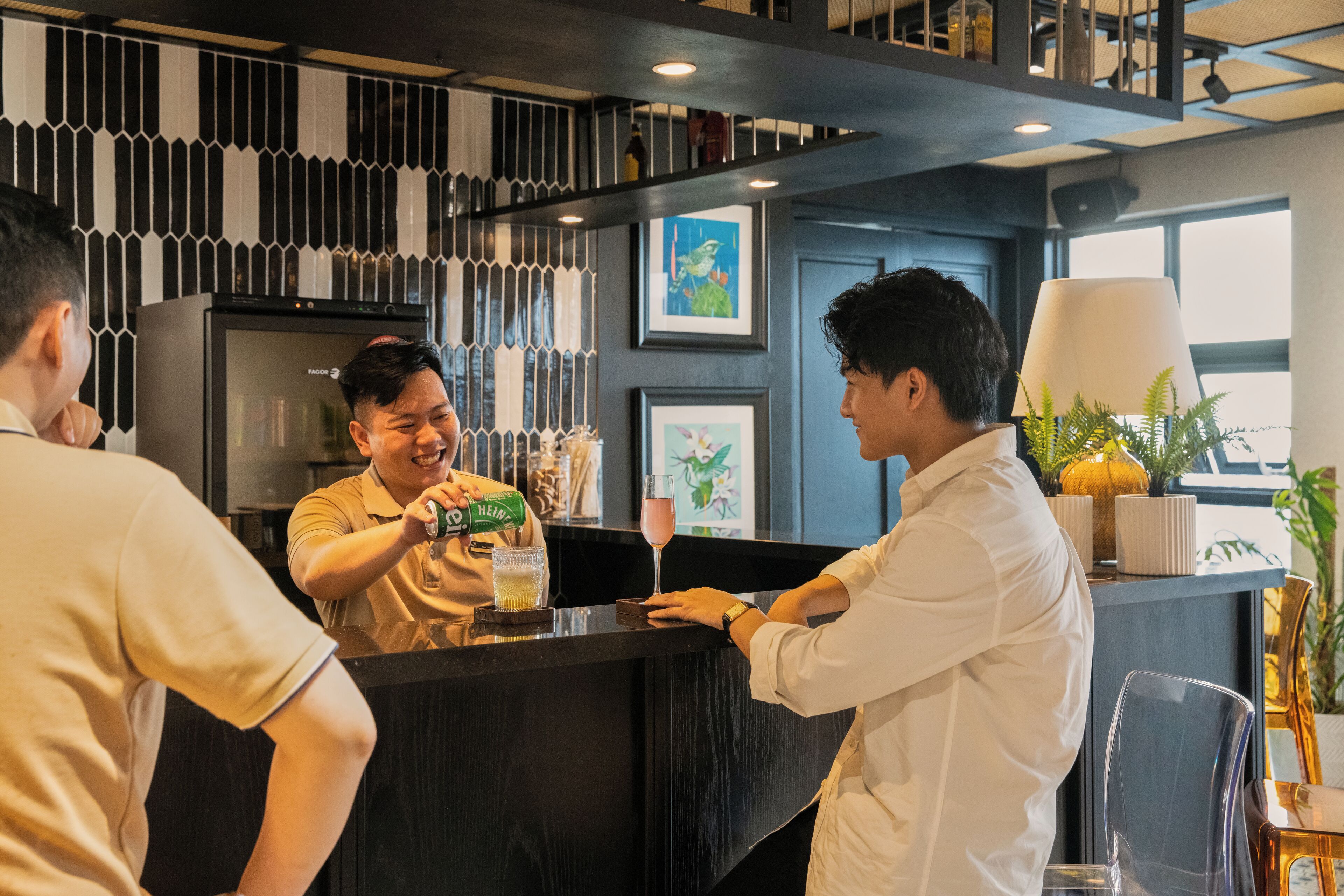 A bar area with a counter, a refrigerator, and framed artwork on the wall.