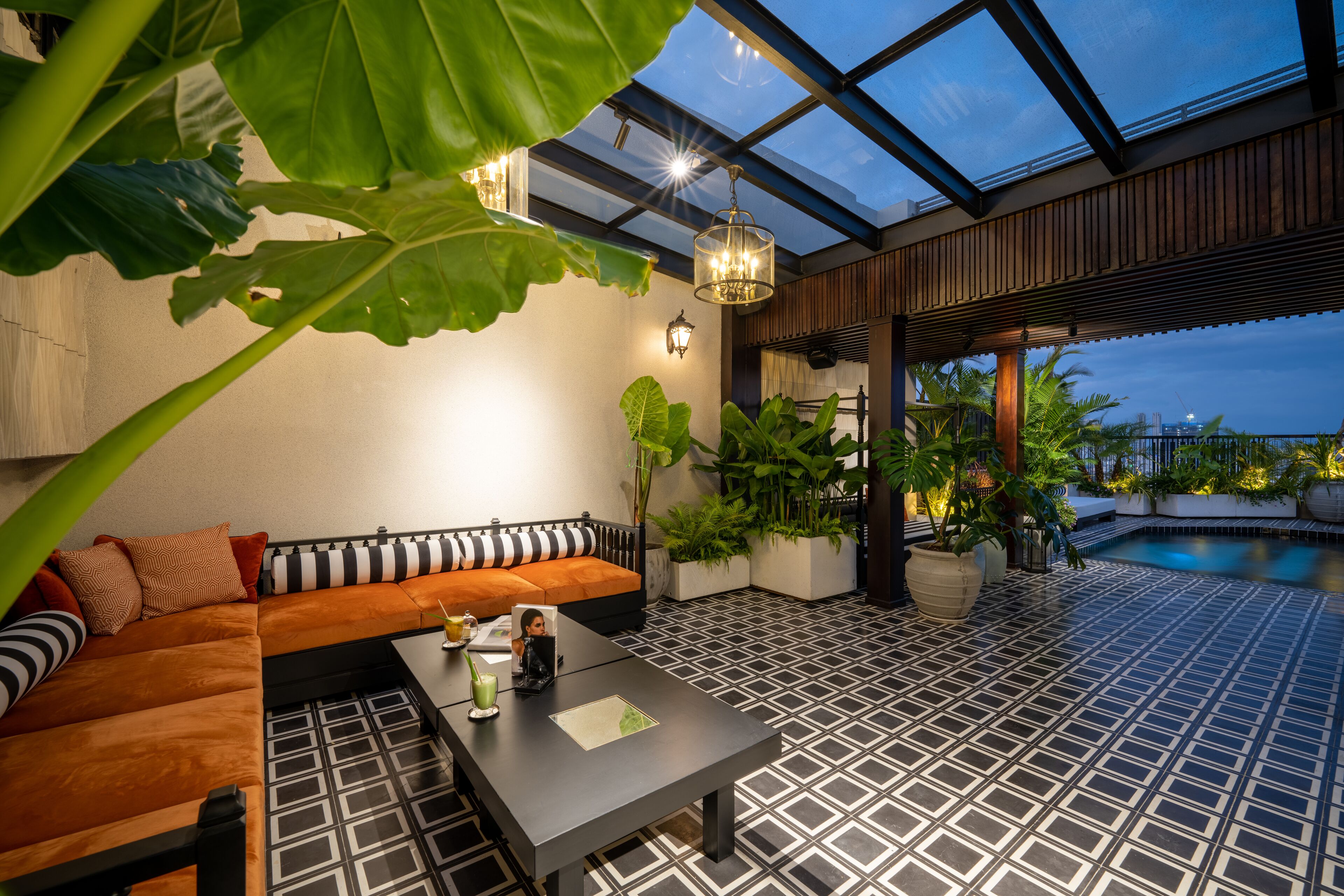 Un espacio lounge exterior moderno con suelo de baldosas blanco y negro, un banco de madera y techo de vidrio.