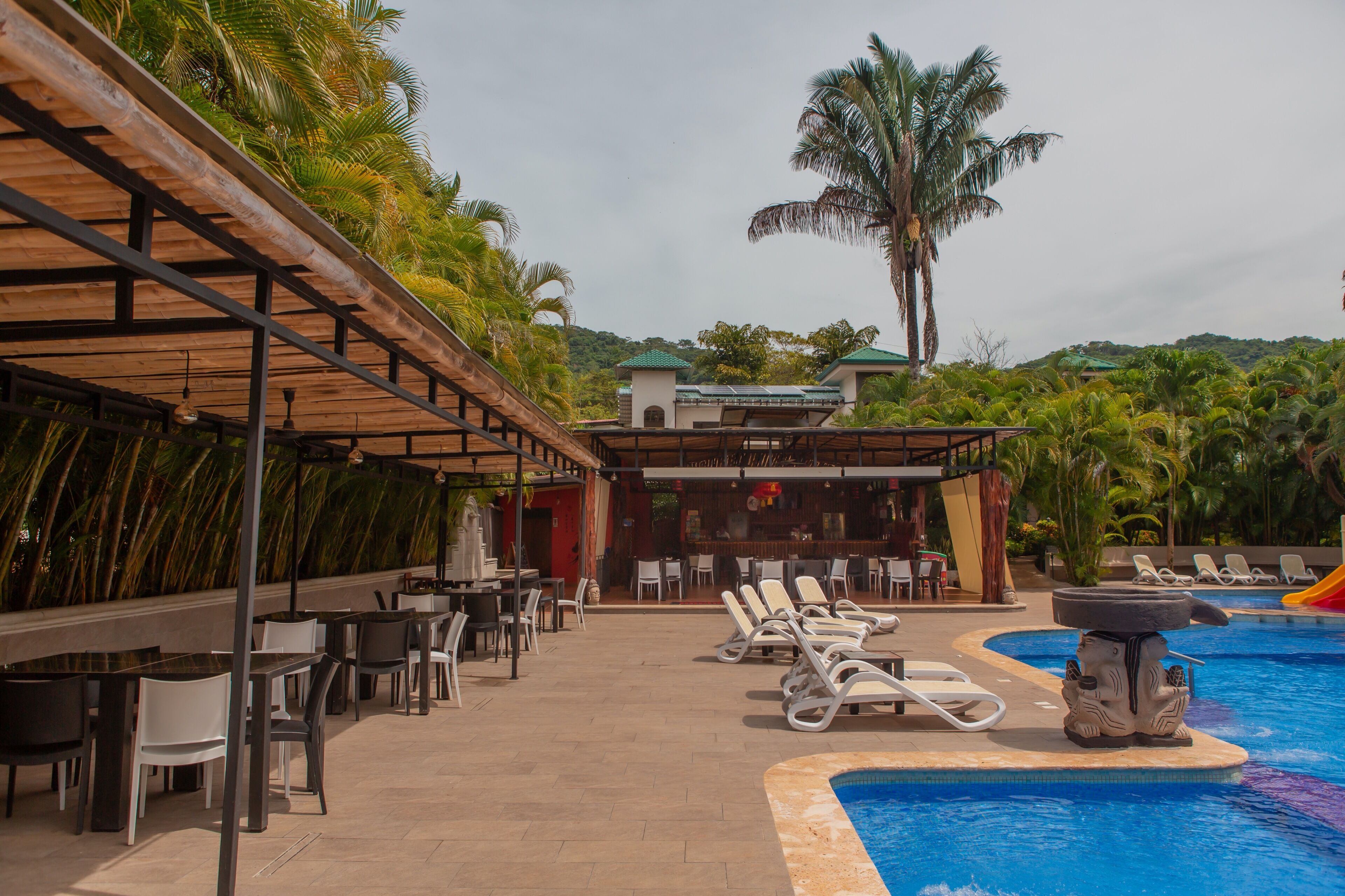 Un área junto a la piscina con sillones reclinables, un bar y una zona de estar cubierta con mesas y sillas.