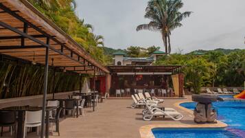 Un área junto a la piscina con sillones reclinables, un bar y una zona de estar cubierta con mesas y sillas.