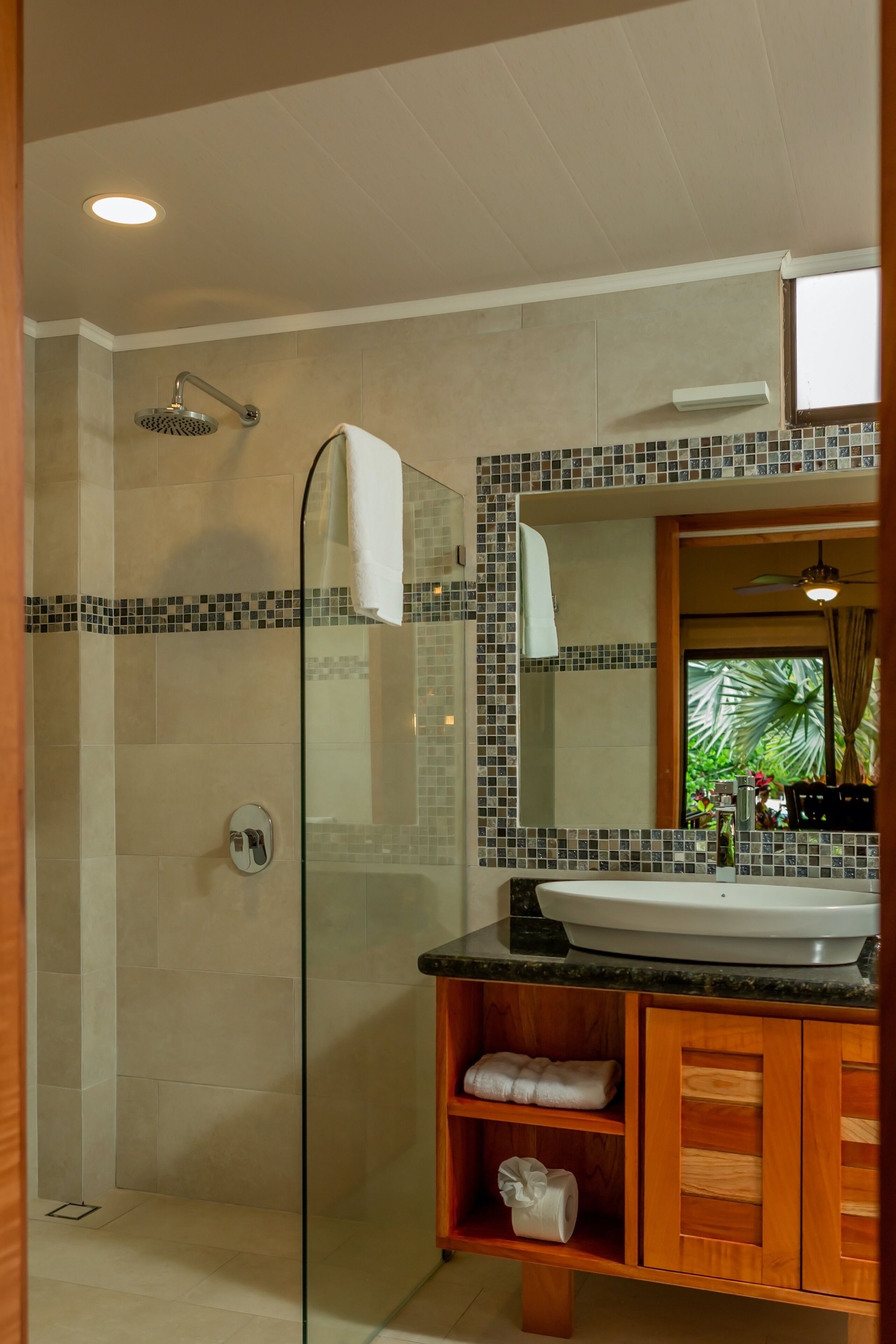A modern bathroom with a glass-enclosed shower, a large mirror, and a wooden vanity with a sink.