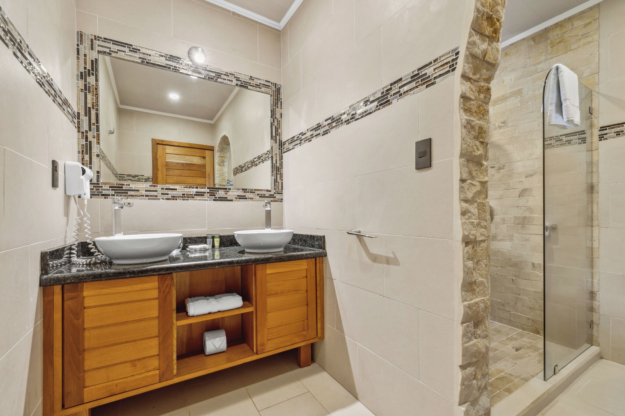 Un baño con dos lavamanos, un espejo, una ducha y armarios de madera.