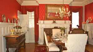 A formal dining room with a fireplace, a chandelier, and red walls. - The Albanus Phillips Inn (Cambridge)
