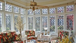 A sunlit room with wicker furniture, a decorative ceiling fan, and large windows with lattice designs. - The Albanus Phillips Inn (Cambridge)