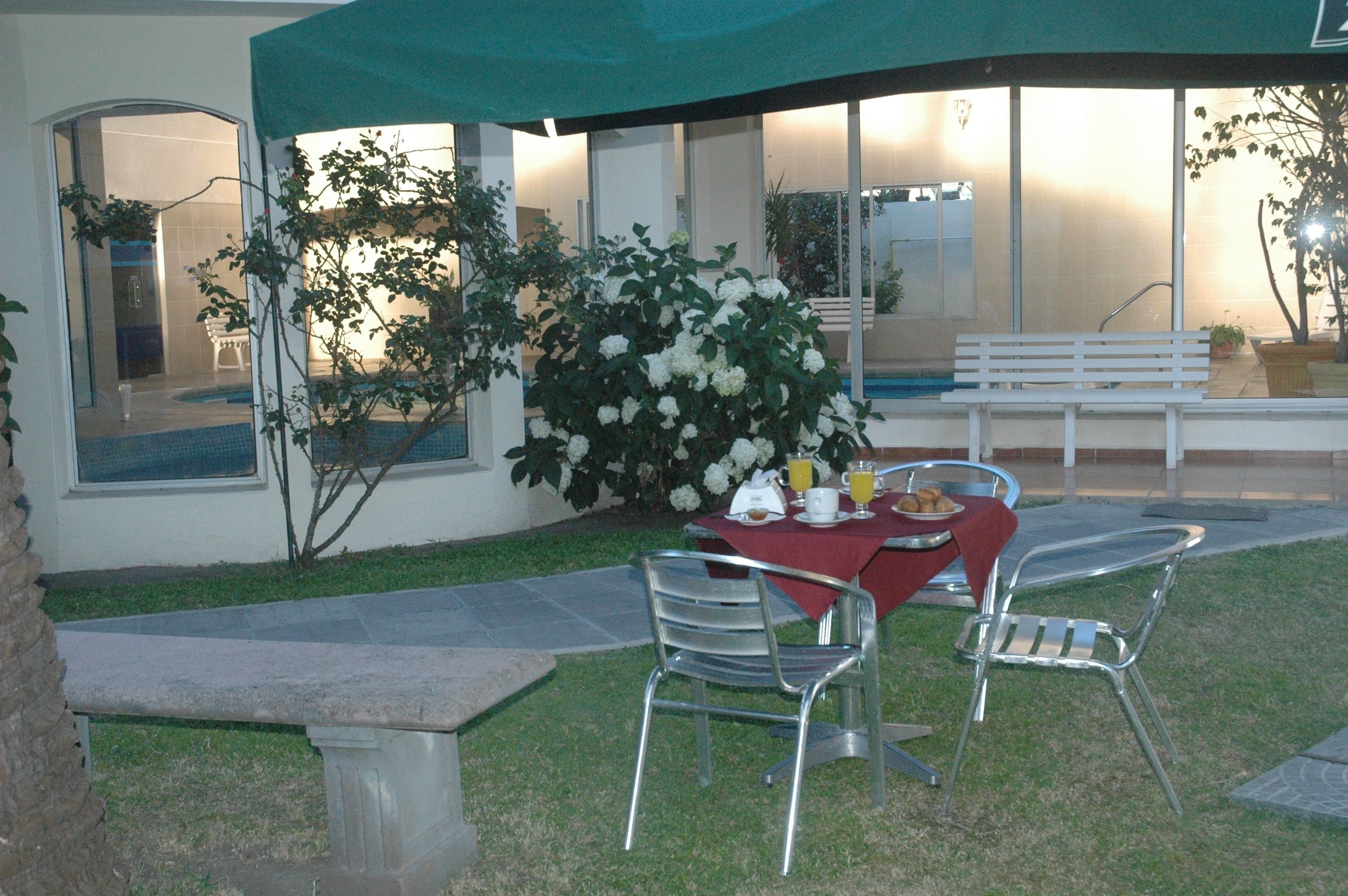 Un espace de restauration en plein air avec une table dressée pour deux personnes, entourée de chaises et d’un banc.