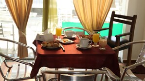 A breakfast table with a red tablecloth, plates of food, cups, and glasses of orange juice.