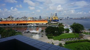 A waterfront view with a large building with an orange roof, boats, and a city skyline in the background. - Watermark Hotel Sizihwan (Kaohsiung)