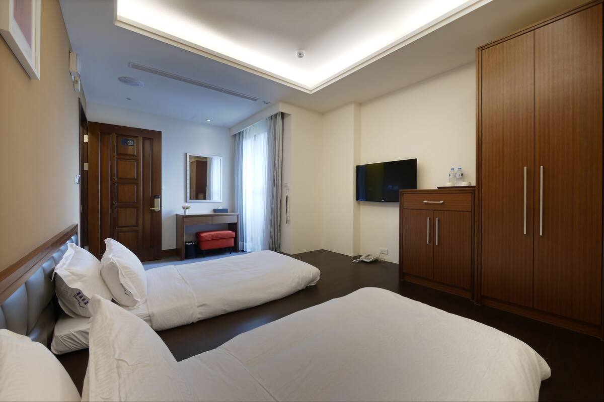 Une chambre d’hôtel avec deux lits, une télévision, une armoire en bois et un bureau avec une chaise.
