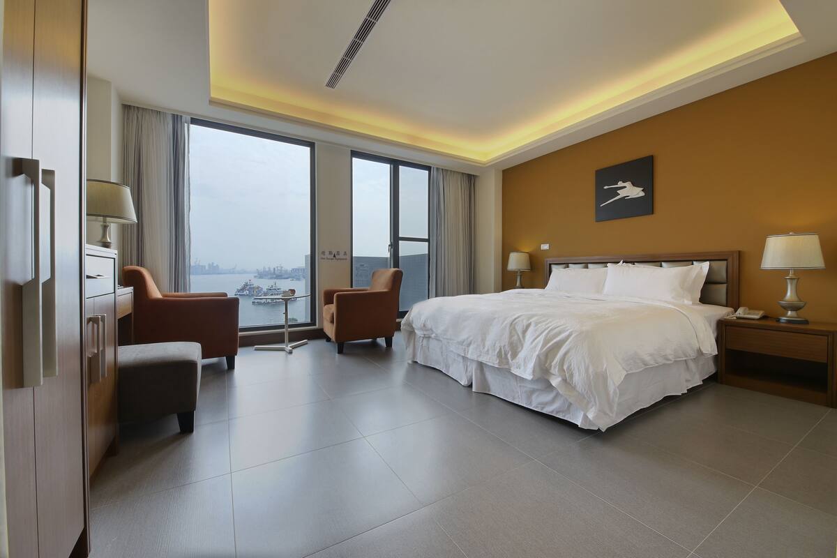 Une chambre d’hôtel comprenant un lit, deux chaises, une table de chevet, une lampe, une fenêtre avec vue et un luminaire au plafond.