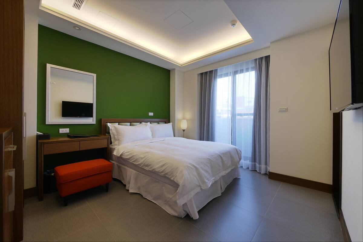 Une chambre d’hôtel avec un lit, un bureau, une chaise, une télévision et une fenêtre avec des rideaux.