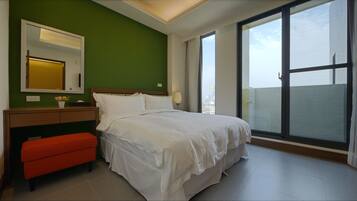 Una habitación de hotel con cama, mesita de noche, espejo, ventana con vistas a edificios y un banco rojo.