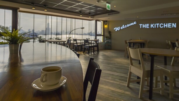 A modern dining area with a view of a river, a 'Welcome' sign, and tables and chairs arranged for dining. - Watermark Hotel Sizihwan (Kaohsiung)