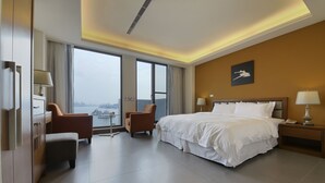 A hotel room with a large bed, two armchairs, a small table, and a view of the city through large windows. - Watermark Hotel Sizihwan (Kaohsiung)