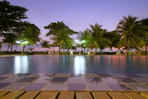 A swimming pool with tiled flooring, surrounded by palm trees and lounge chairs. - Hotel Pangeran Beach (Padang)