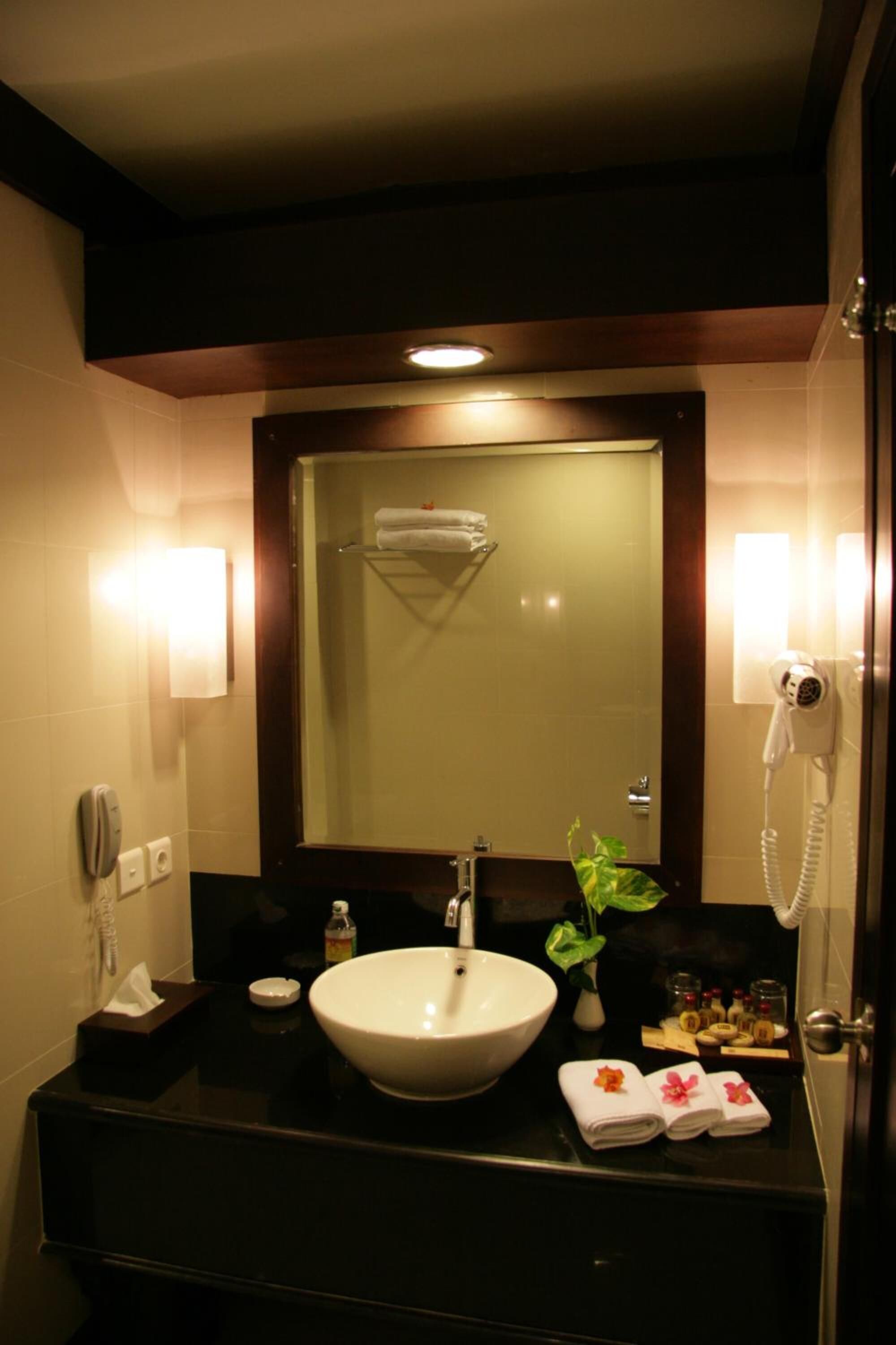 A hotel bathroom with a large sink, a mirror, a hairdryer, and a telephone.