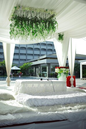 An outdoor wedding setup with a white canopy, hanging floral arrangements, and a stage with a microphone. - Hotel Pangeran Beach (Padang)