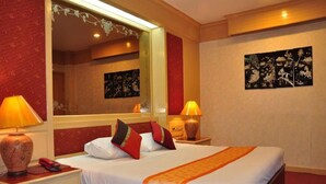 A hotel room with a large bed, two bedside tables with lamps, a mirror, and artwork on the walls. - Parkway Inn (Bangkok)