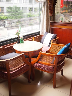 A cozy seating area with a round table and wicker chairs, a small vase with flowers, and a bottle of beer on the windowsill. - Parkway Inn (Bangkok)