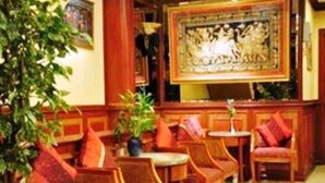 A lobby with wooden chairs and tables, a large decorative wall piece, and potted plants. - Parkway Inn (Bangkok)