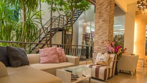 A modern living room with a sofa, armchair, and coffee table. There is a staircase with a railing, and a brick pillar. - Phuket Jula Place (Chalong)