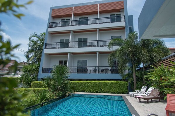 A modern multi-story hotel with a swimming pool, outdoor seating, and lush greenery. - Phuket Jula Place (Chalong)