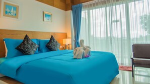 A hotel room with a large bed, wooden ceiling, two framed pictures, a blue curtain, and a chair. - Phuket Jula Place (Chalong)